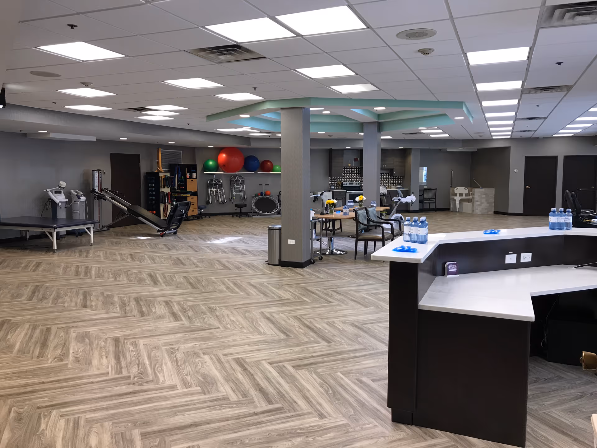 Large open interior therapy and activity room with exercise equipment, therapy balls, tables and a reception desk.