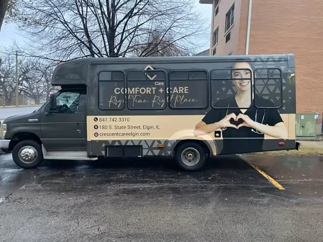 A Crescent Care shuttle van parked outside a brick building with large promotional graphics, a smiling caregiver image, and contact information on its side.