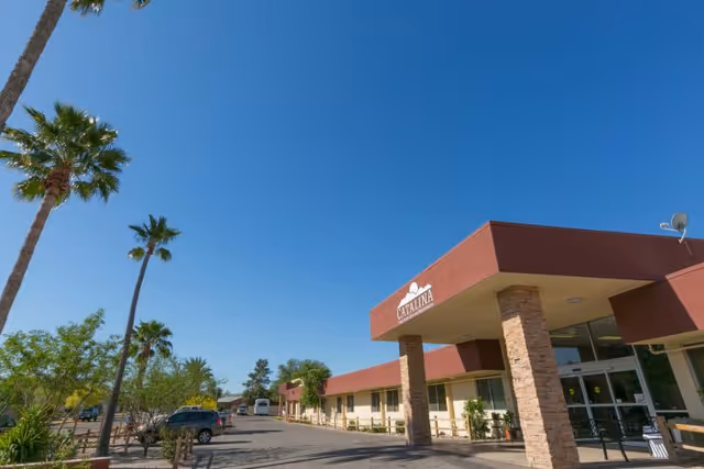 Exterior view of Catalina Post Acute And Rehabilitation facility under a clear blue sky with palm trees and parked cars along the driveway.