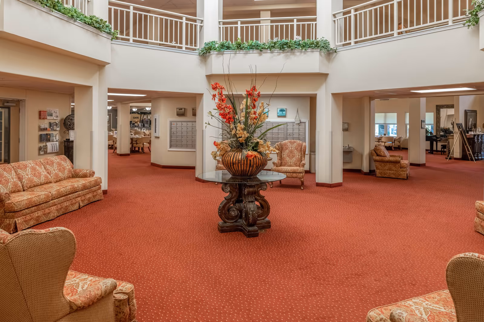 Spacious two-story interior lobby with red carpet, upholstered seating and a central table topped with a floral arrangement.