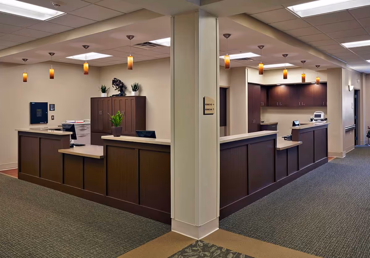 Reception desk area with dark wood counters, pendant lights, and cabinets in a senior living facility.