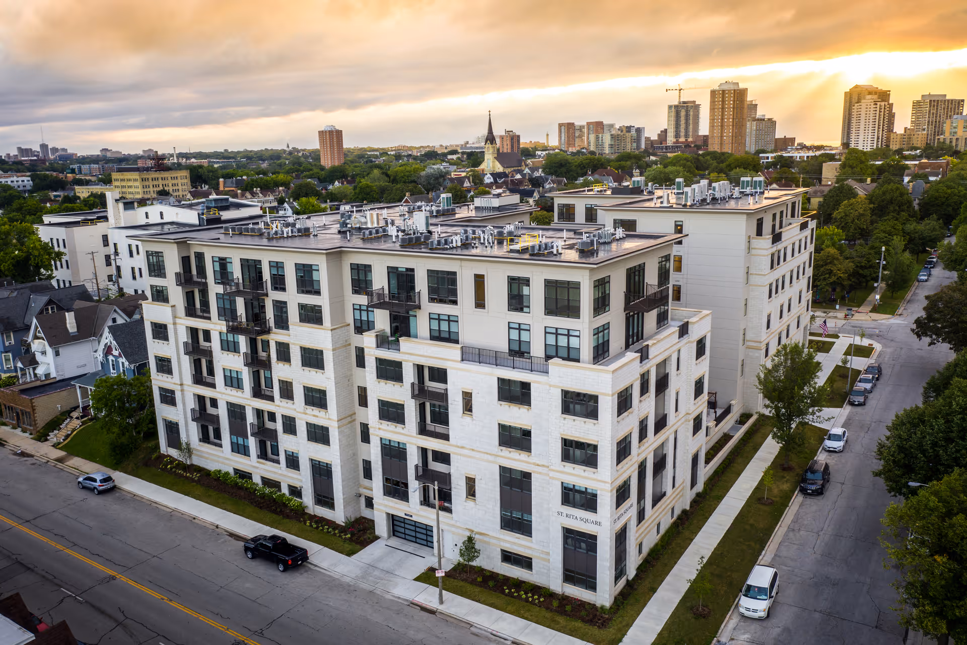 Aerial view of the St. Rita Square multi-story residential building and surrounding neighborhood at sunset.