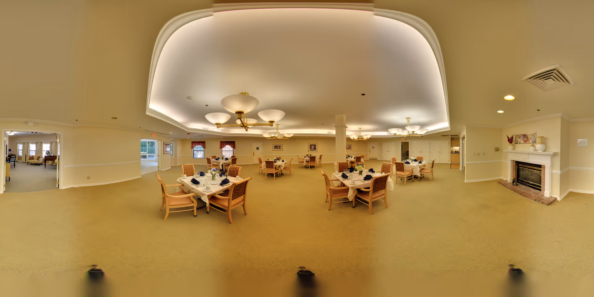 Large dining room with several set tables and chairs under decorative ceiling lights and a fireplace on the right.