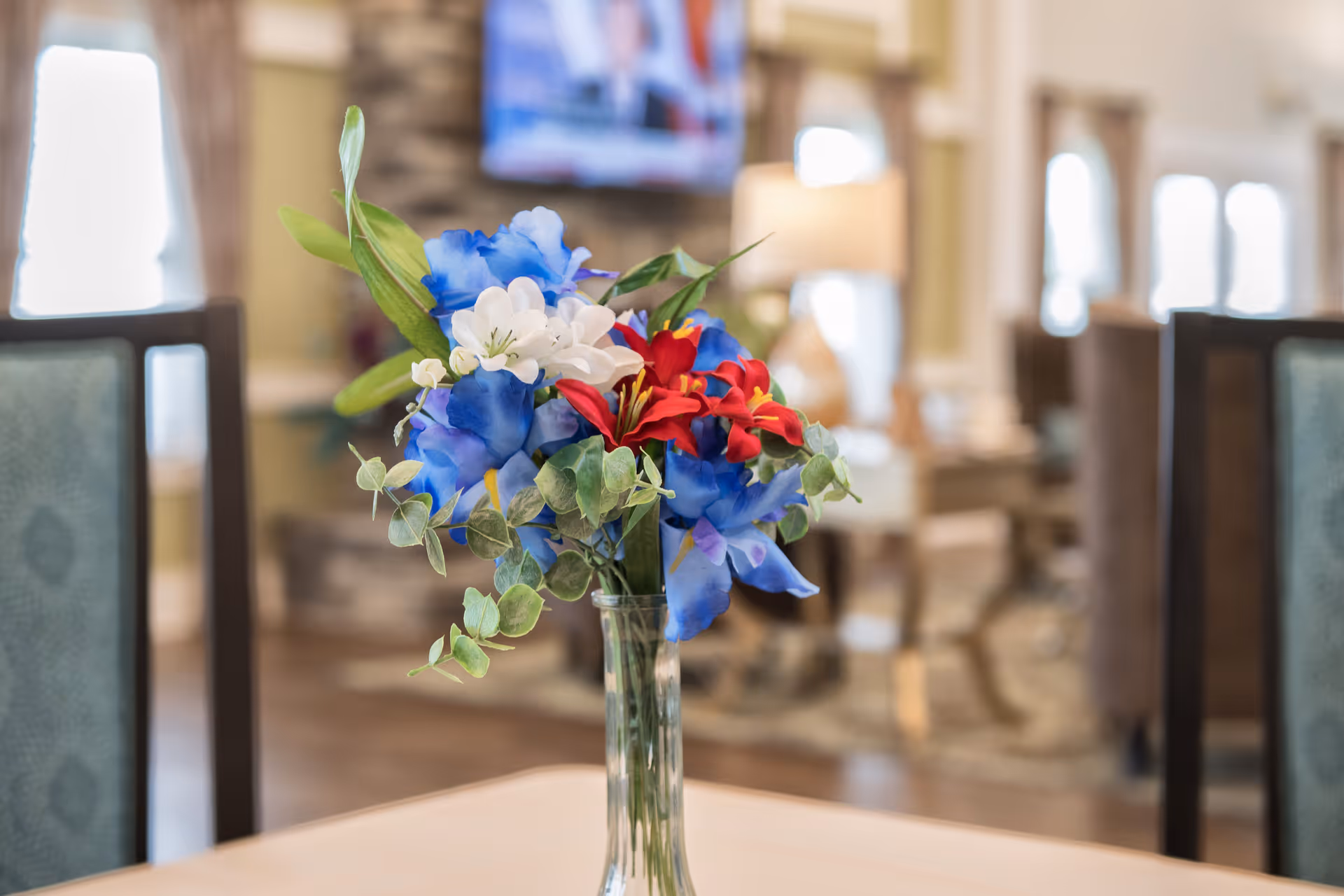 A vase of blue, red, and white flowers on a table in a softly lit communal dining area.