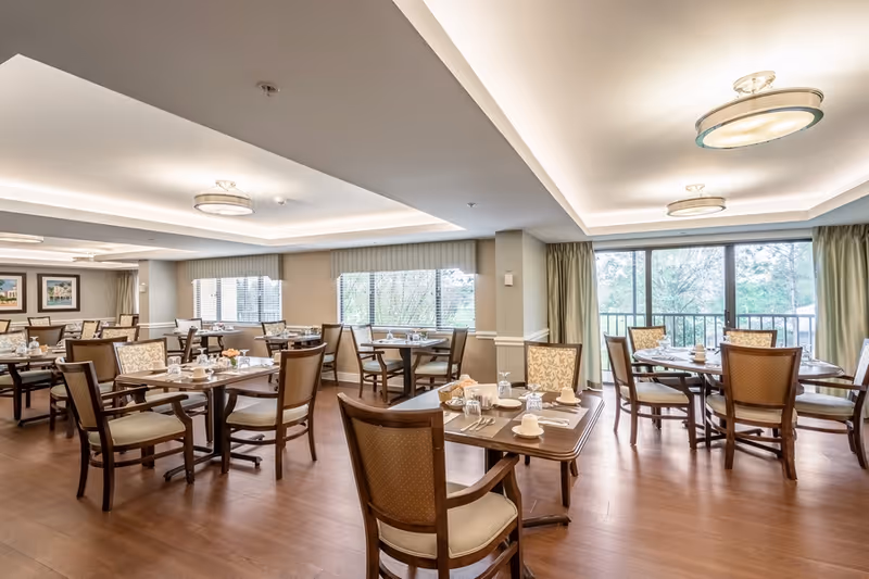 Spacious, well-lit dining room with multiple set tables and chairs, wood flooring, and large windows.