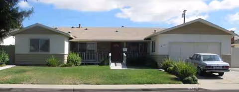 Single-story residential facility with a manicured front yard, walkway, and parked car.