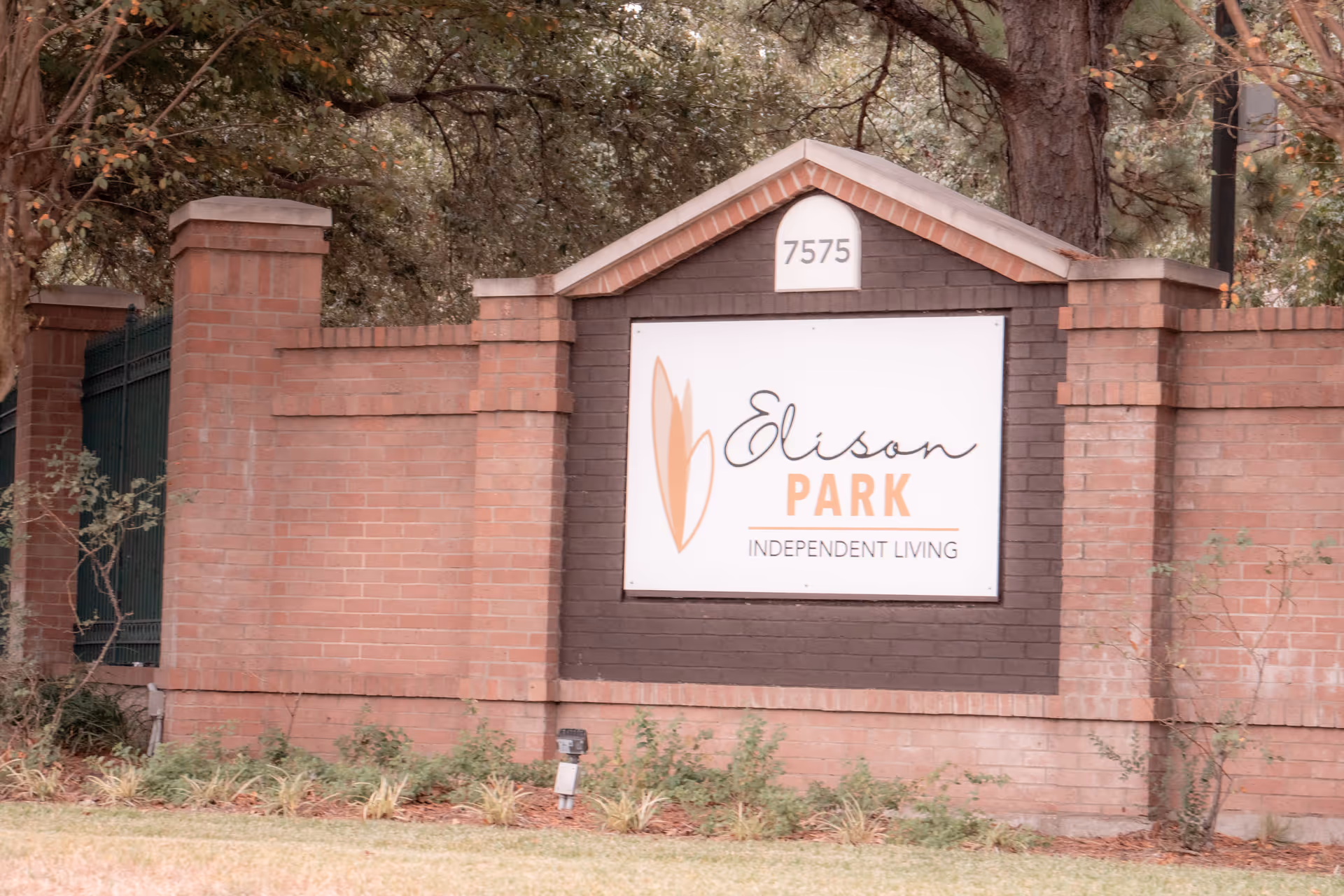 A brick entrance sign for Edison Park Independent Living with the address number 7575 displayed above. The sign is surrounded by trees and landscaping.