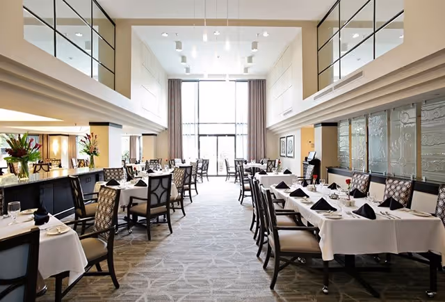 Bright, elegant dining room with neatly set tables, high ceilings and large windows.