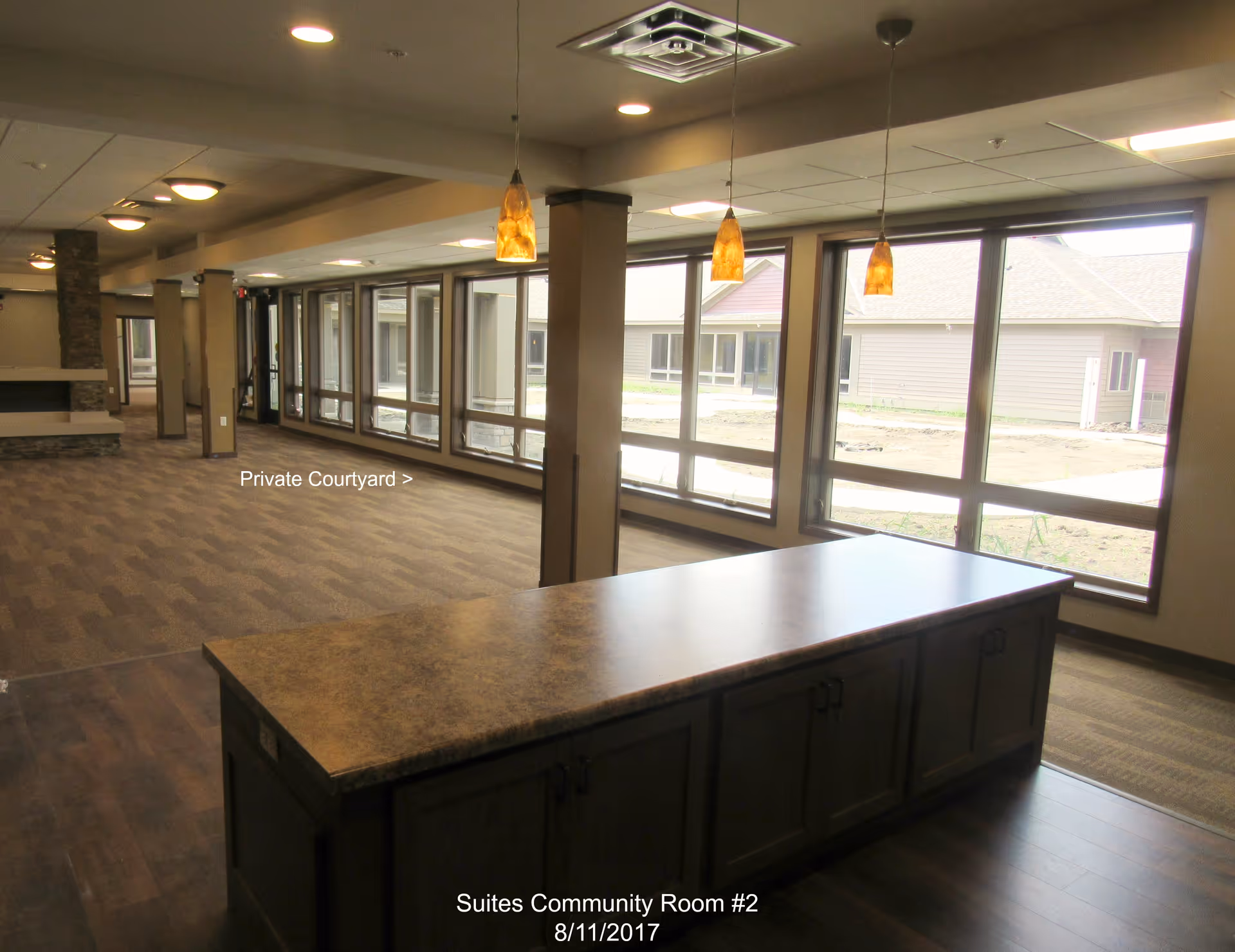 Spacious community room with a large island counter, pendant lights, and floor-to-ceiling windows overlooking a courtyard.