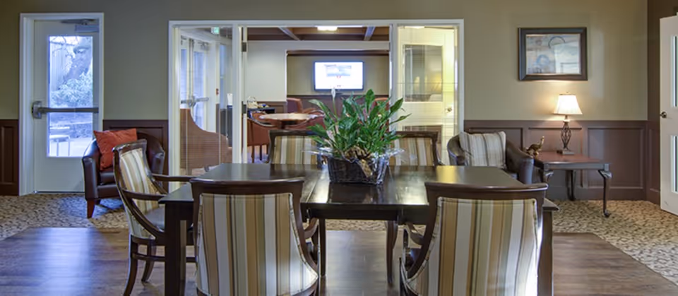Communal dining area with a wooden table, striped upholstered chairs, a potted plant centerpiece, seating alcoves, and a TV on the far wall.