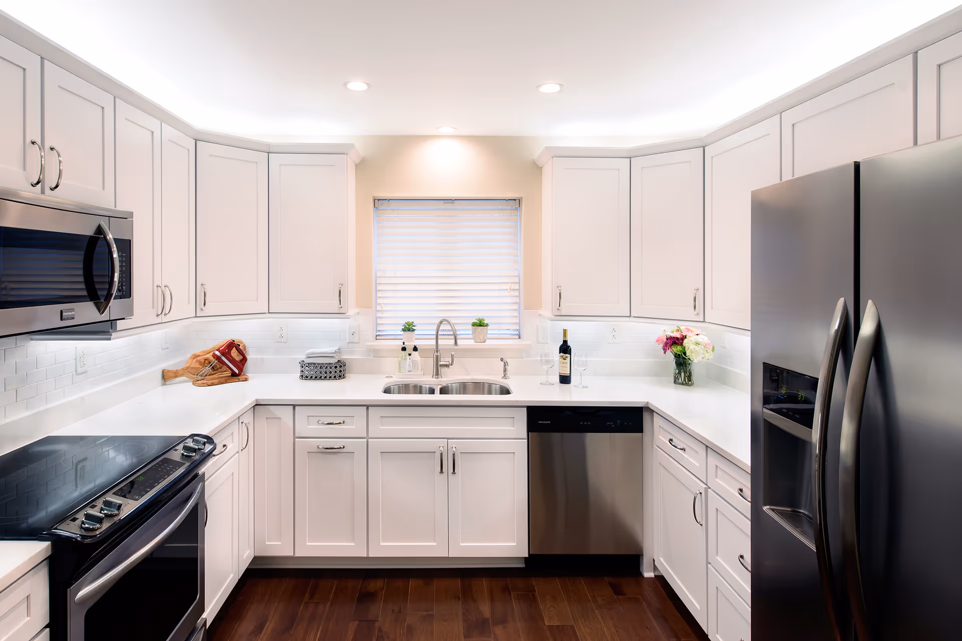 Bright modern kitchen with white cabinetry, stainless steel refrigerator, oven and dishwasher, and a sink beneath a window.