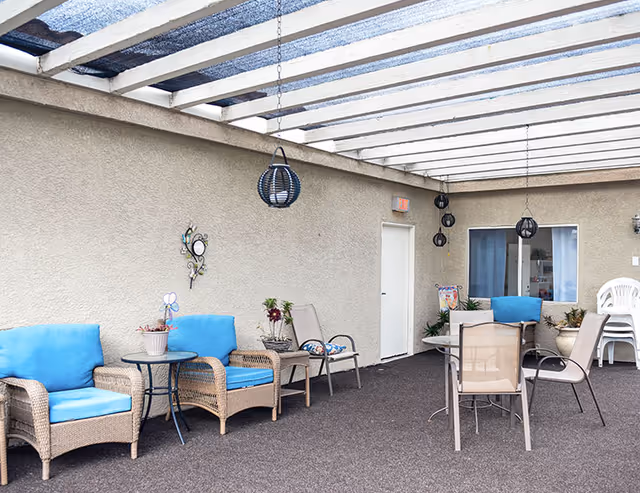 Covered outdoor patio with wicker chairs and blue cushions, tables, hanging lanterns, and potted plants.
