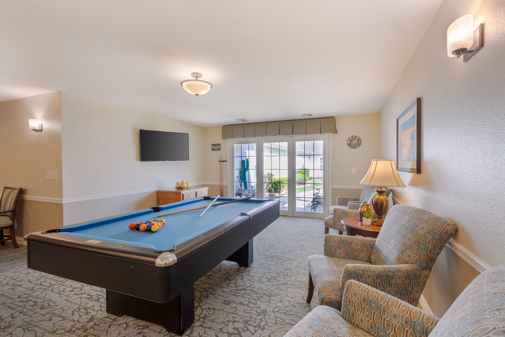 Common sitting room featuring a pool table, armchairs and a wall-mounted TV with glass doors leading to an outdoor patio.