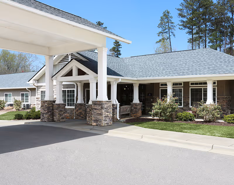 Exterior view of a senior living facility entrance with a covered driveway and stone pillars.