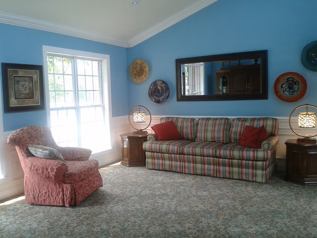 Sunlit living room with a striped sofa, red upholstered armchair, side tables with lamps, a large mirror and blue walls.