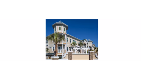 Exterior view of a multi-story senior living building with palm trees under a clear blue sky.
