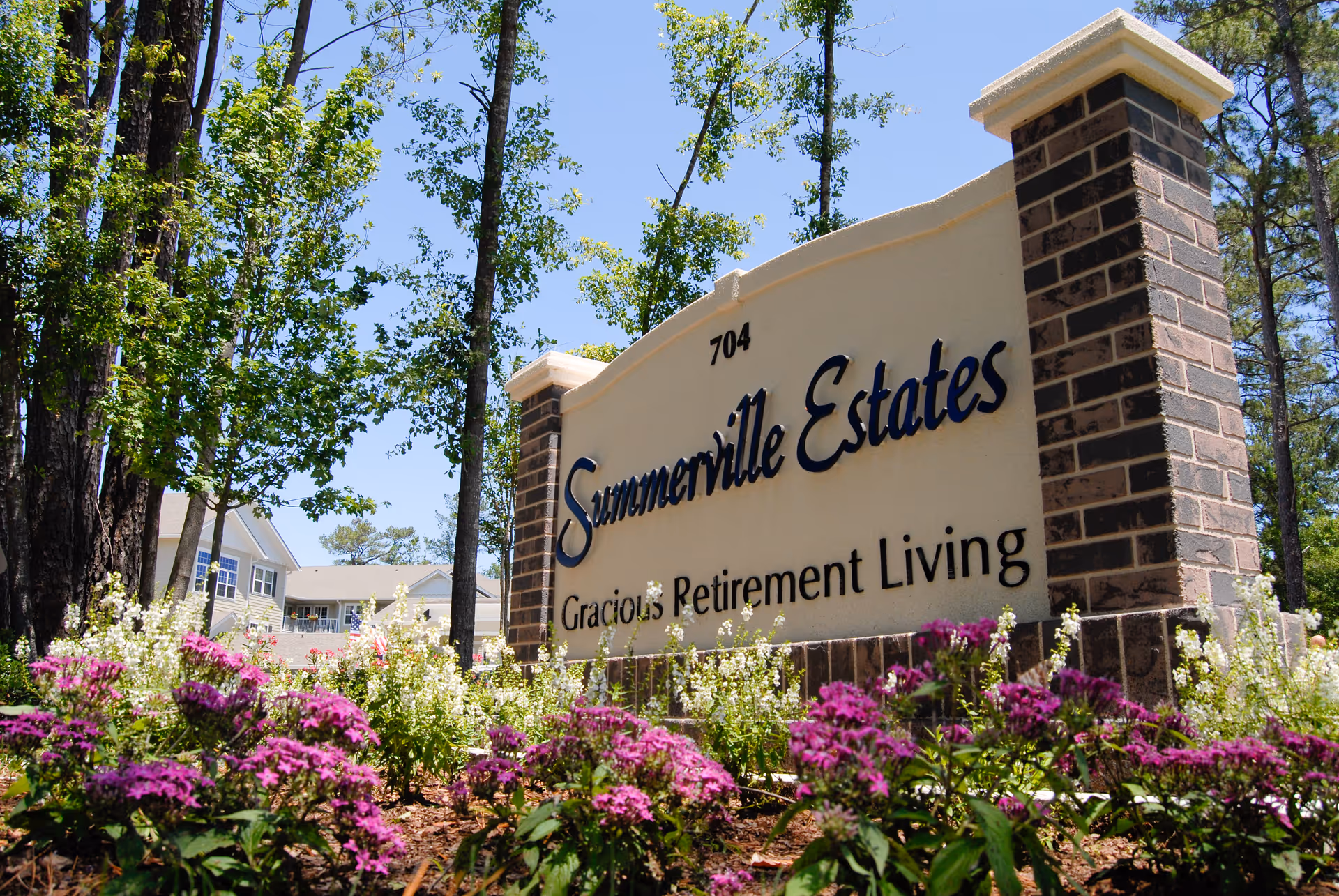 Sunlit exterior sign reads Summerville Estates Gracious Retirement Living amid flowering landscaping.