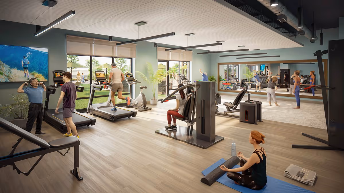A bright and spacious fitness room with several people exercising. The room features treadmills, weight machines, and a large mirror on one wall. A woman is sitting on a yoga mat meditating in the foreground, while others use the equipment or stretch. Large windows provide a view of an outdoor area with green grass and umbrellas.