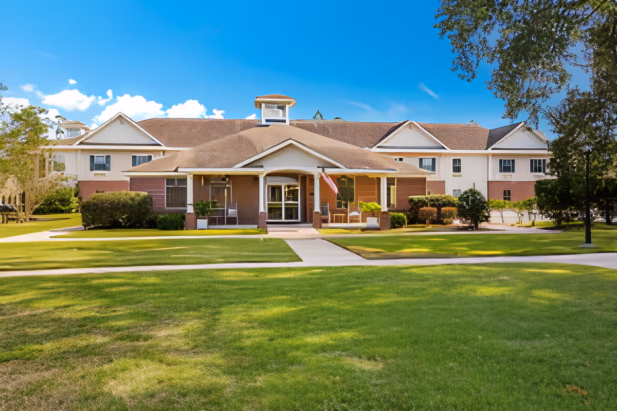 Front exterior of a two-story senior living facility with a covered entrance, American flag, and wide green lawn.