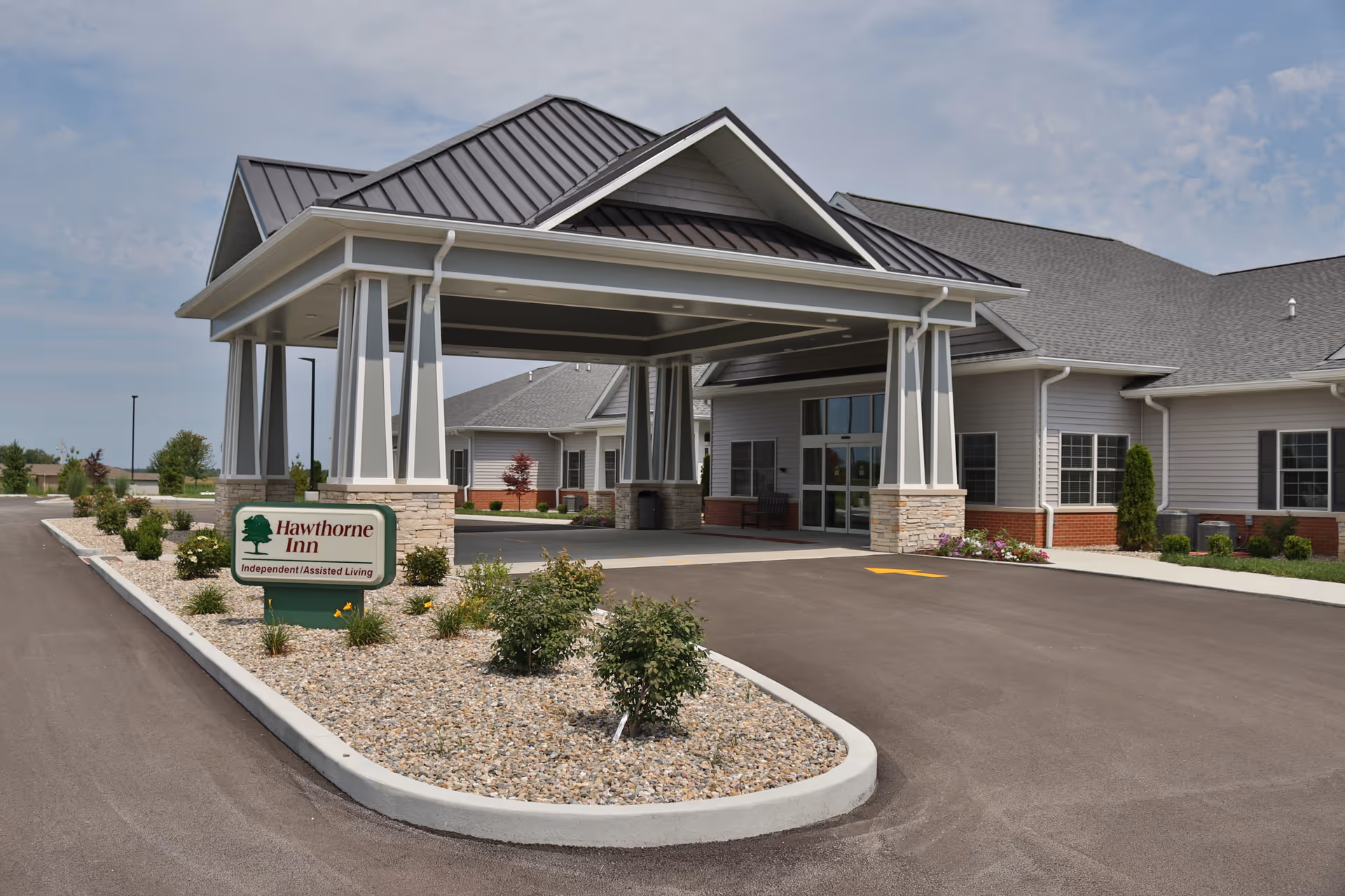 Covered porte-cochère and main entrance of a single-story senior living facility with a landscaped median and a 'Hawthorne Inn' sign.