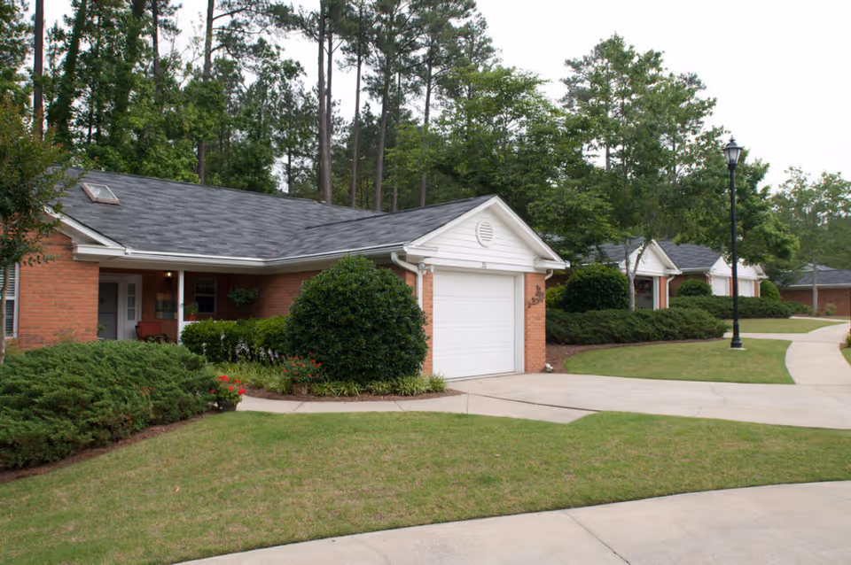 Single-story brick cottage-style senior living units with garages, shrubs, and a curved driveway.