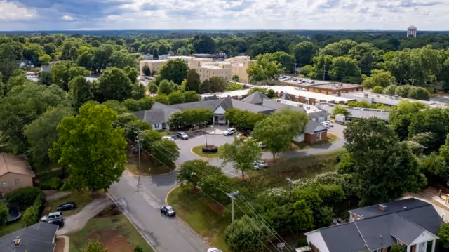 Aerial view of Rock Hill Post Acute Care Center surrounded by trees and residential buildings under a partly cloudy sky.