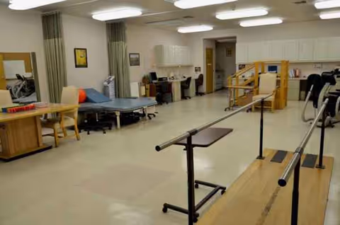 Senior care facility rehab gym with therapy equipment, mats, and parallel bars.