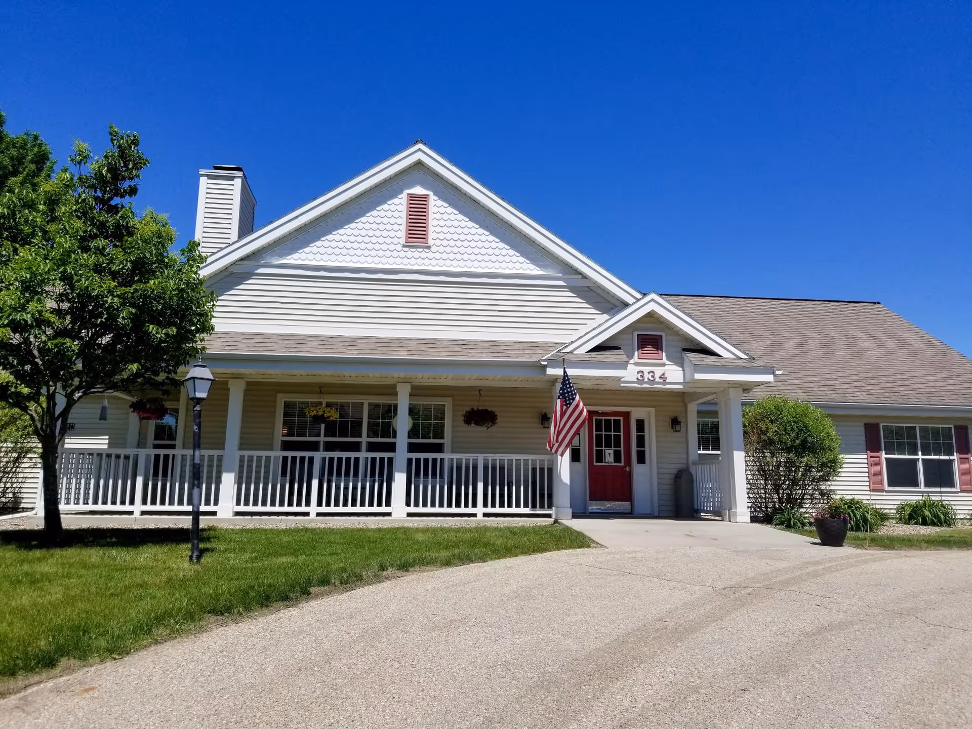 Front view of a single-story building with a long porch, white railing, and American flag.