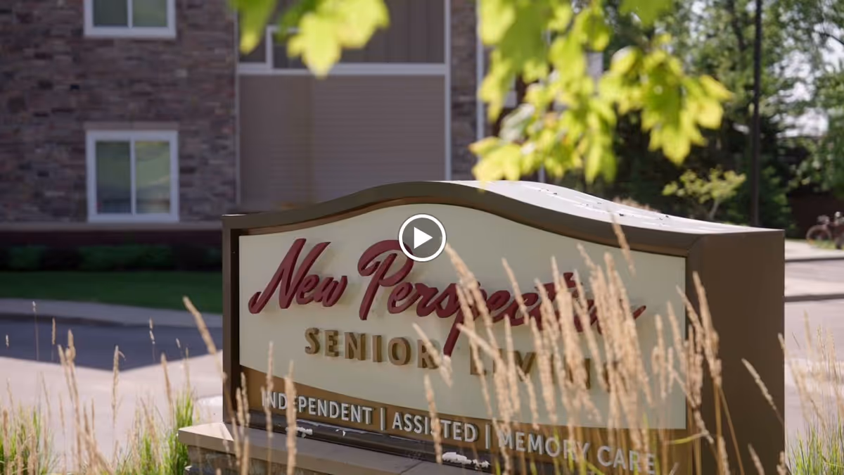 Outdoor view of a sign for New Perspective Senior Living with a building and greenery in the background.