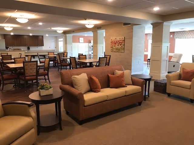 Open communal living and dining area with sofas, armchairs, multiple dining tables and a kitchen counter in the background.