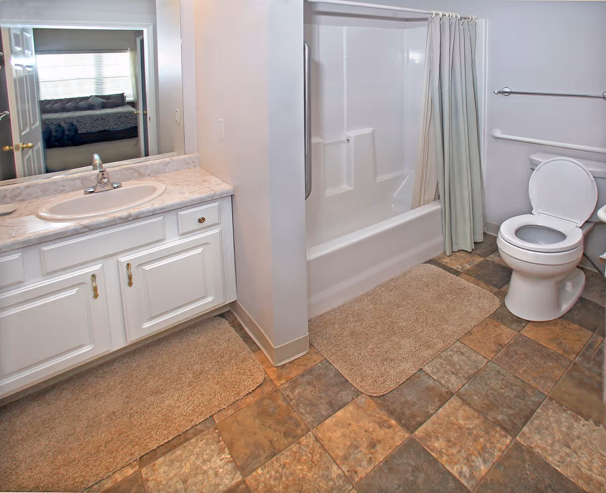 Bathroom with a sink vanity, bathtub with shower curtain, and toilet on a tiled floor.