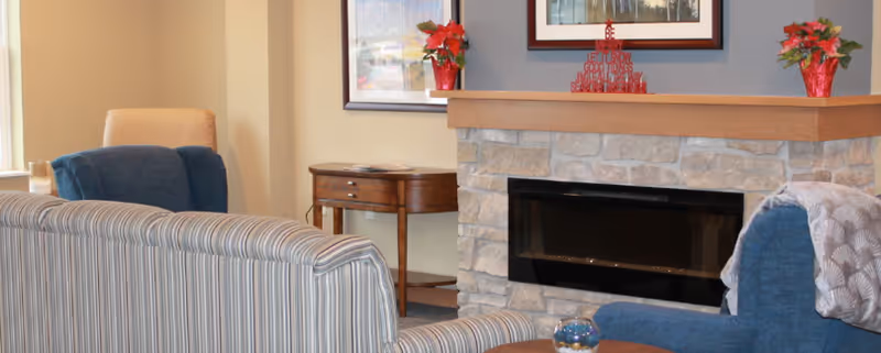 Cozy living room with a striped sofa, blue armchairs, a stone fireplace and small side tables with decorative plants.