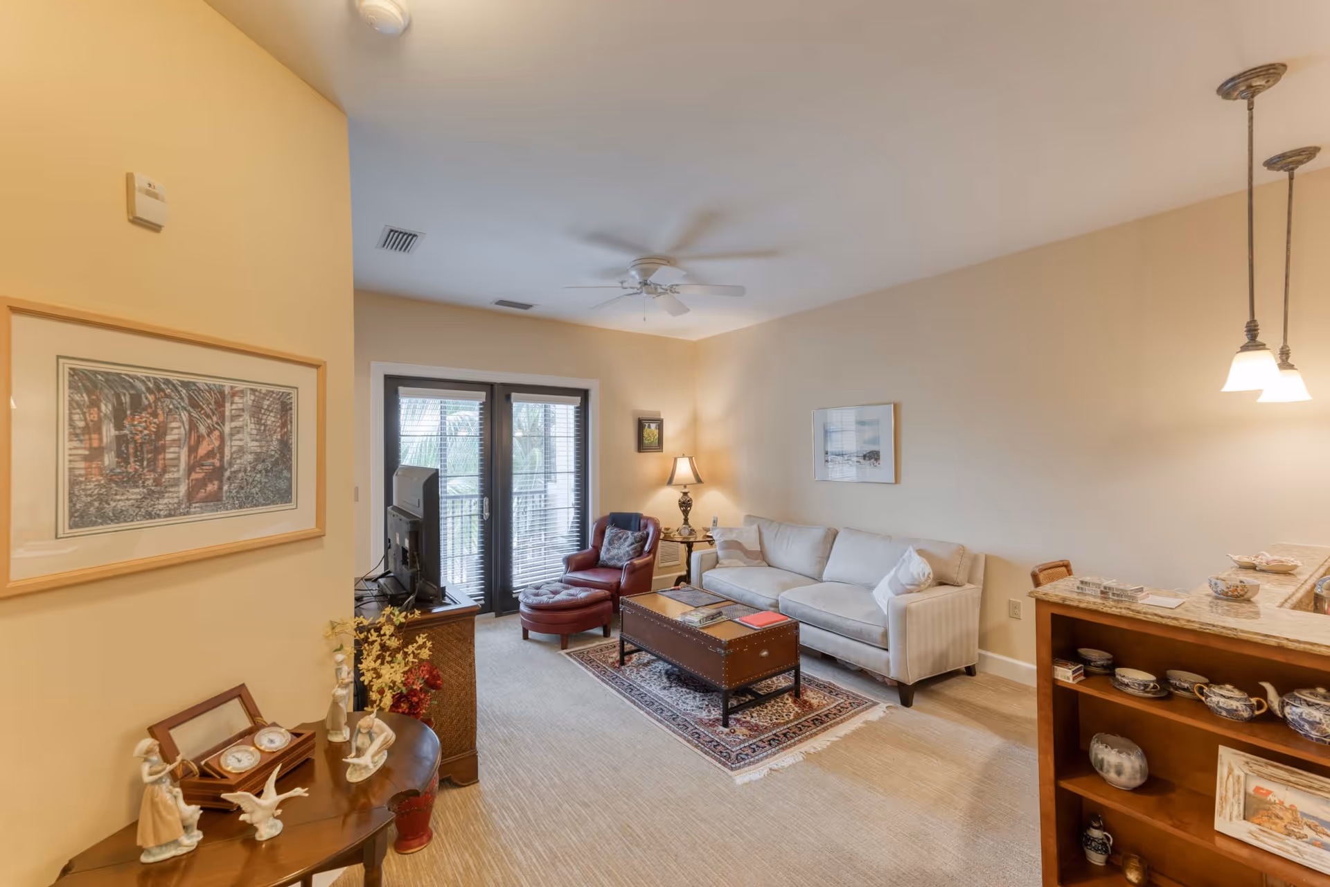 Well-lit living room with a sofa, coffee table, armchair, TV, and French doors leading to a balcony.