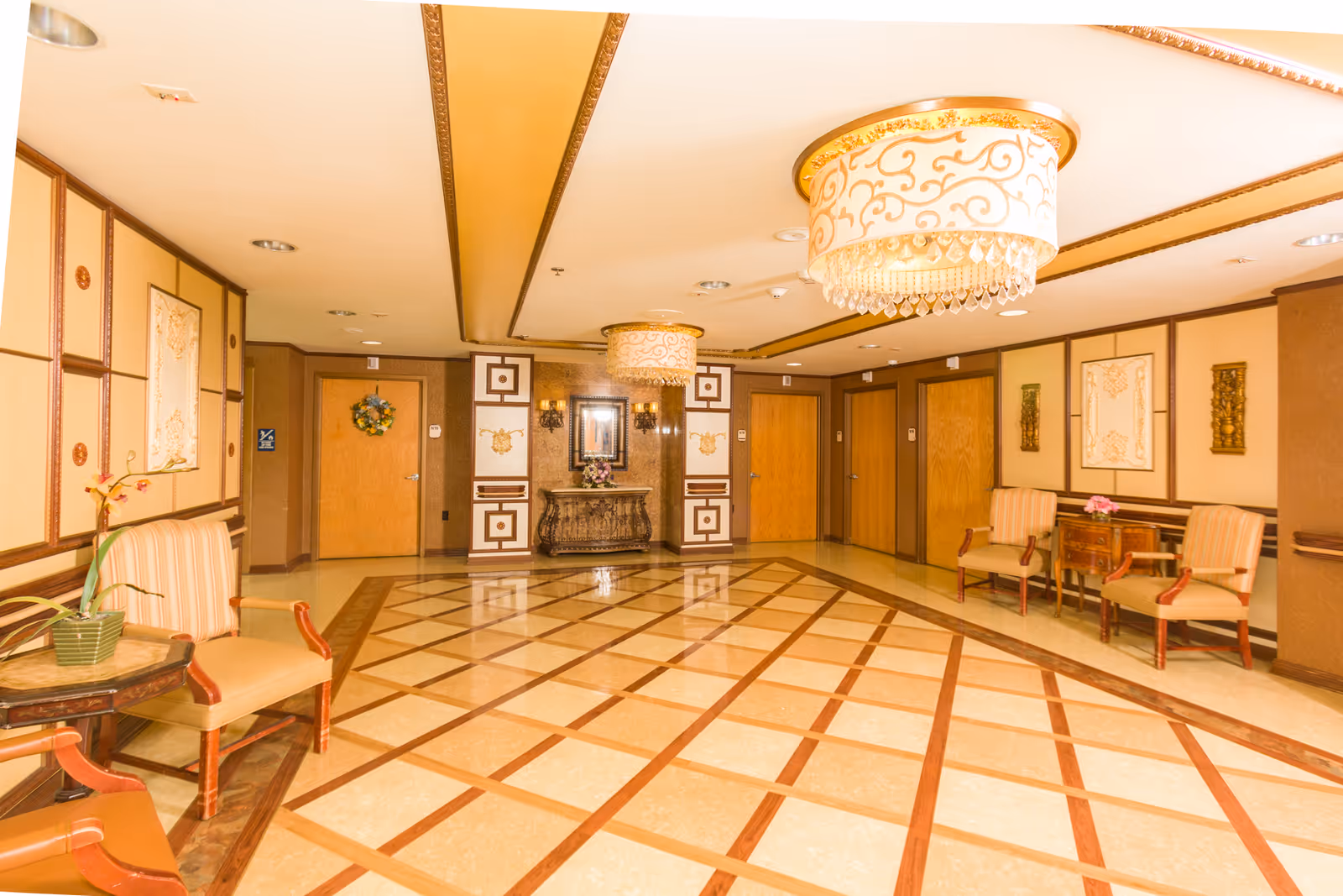 Ornately decorated interior lobby with chandeliers, patterned tile floor, seating and wooden doors.