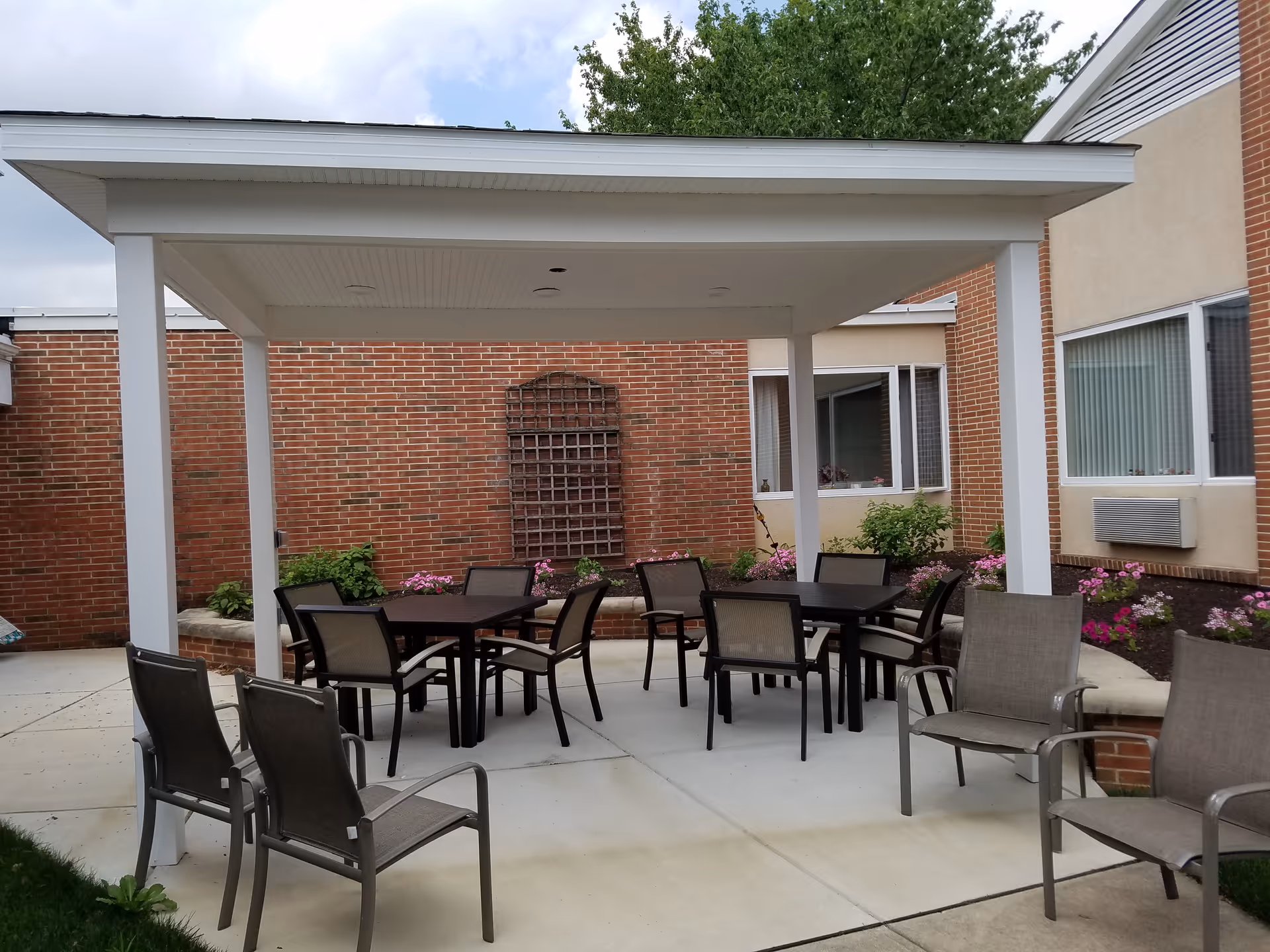 Covered outdoor patio in a brick-walled courtyard with tables and chairs under a white pergola.