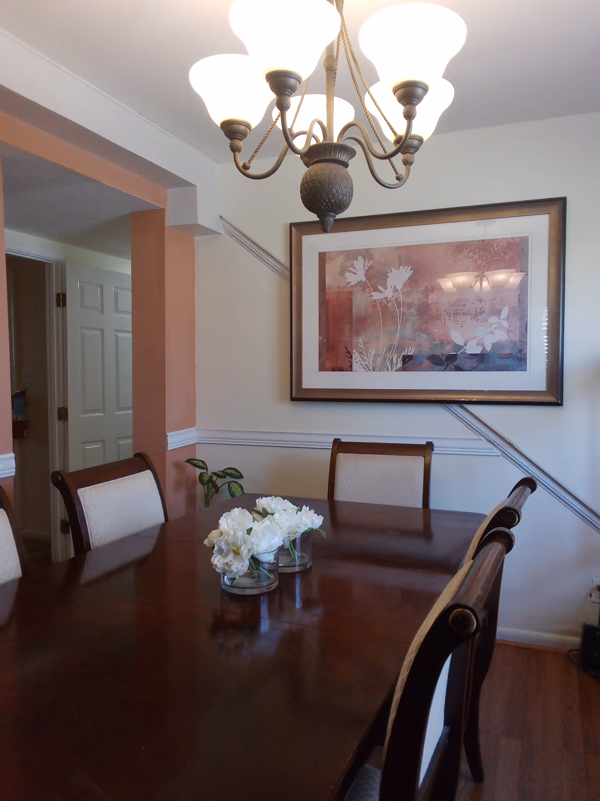 Wood dining table with upholstered chairs in a dining room, chandelier overhead