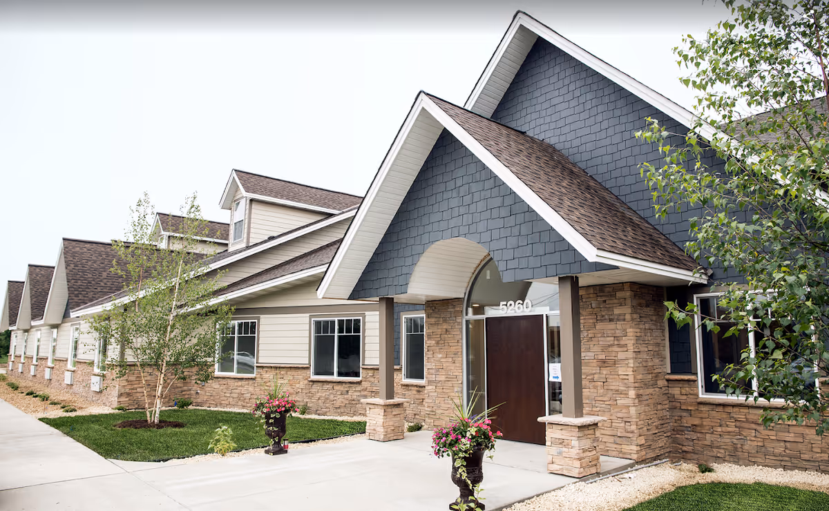 Exterior view of Good Life Senior Living Hugo entrance with peaked roof and stone facade.