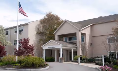 Exterior view of Blenheim-Newport senior living facility with entrance, flag, and landscaping.