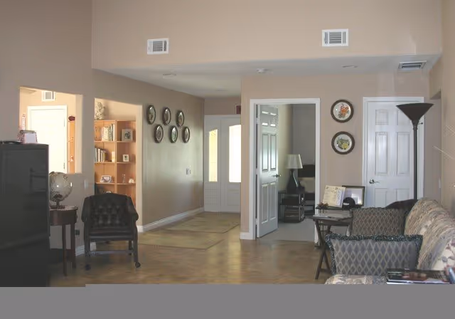 Spacious common living area with a sofa, armchairs, bookshelves, wall decorations, and doorways to adjacent rooms.