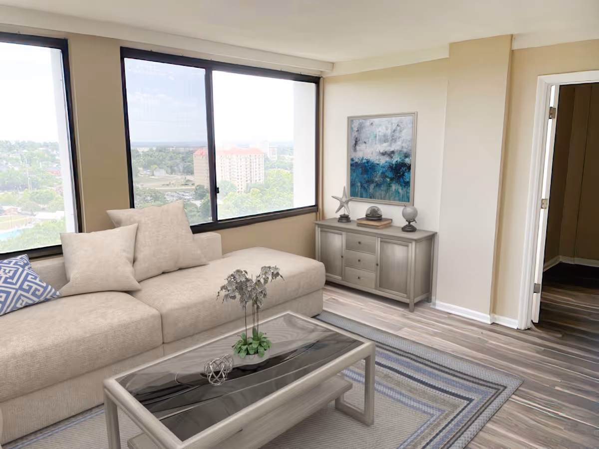 A bright living room with large windows showing a cityscape outside. The room features a beige sectional sofa with multiple cushions, a glass-top coffee table with a small plant and decorative object, a sideboard with decorative items including a starfish sculpture and a framed abstract painting on the wall. The floor has a striped area rug and wood-look flooring.