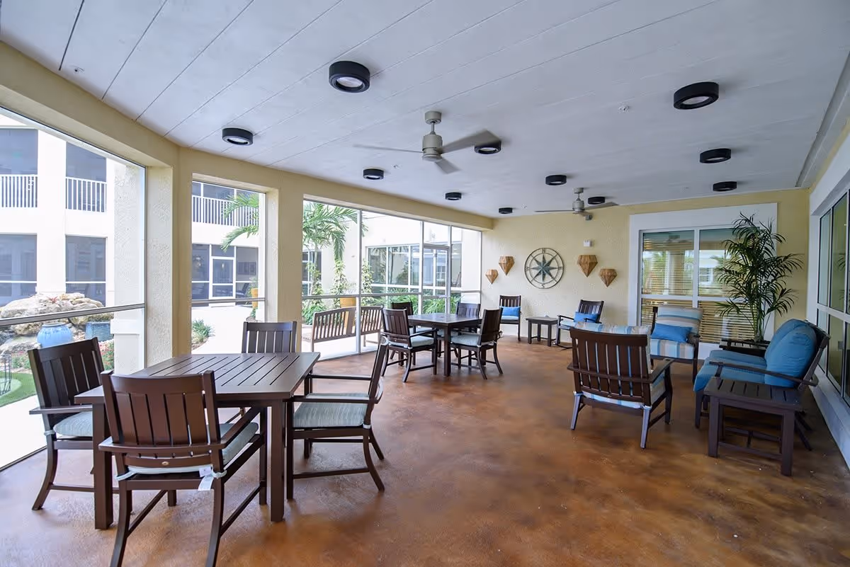 Screened covered patio lounge with tables, chairs, cushioned seating and ceiling fans overlooking a courtyard.