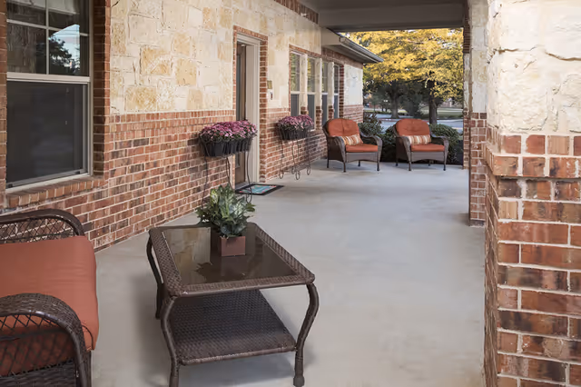 Covered brick and stone front porch with wicker seating, a glass-top coffee table, and potted flowers.