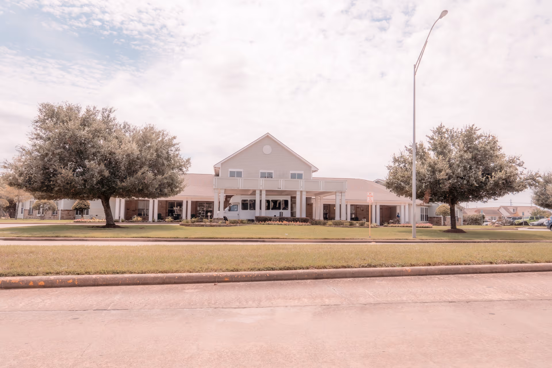 Front exterior of a two-story assisted living and memory care building with a covered entrance, lawn, and trees.