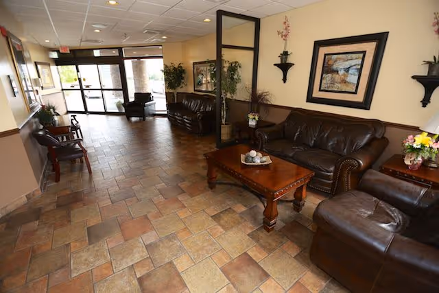 Lobby with leather sofas, a coffee table, tiled floor, plants, and glass entrance doors.