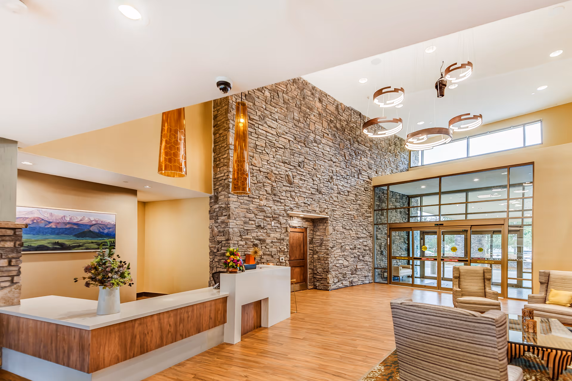 Spacious lobby with a stone accent wall, reception desk, seating area, and large glass entrance doors.