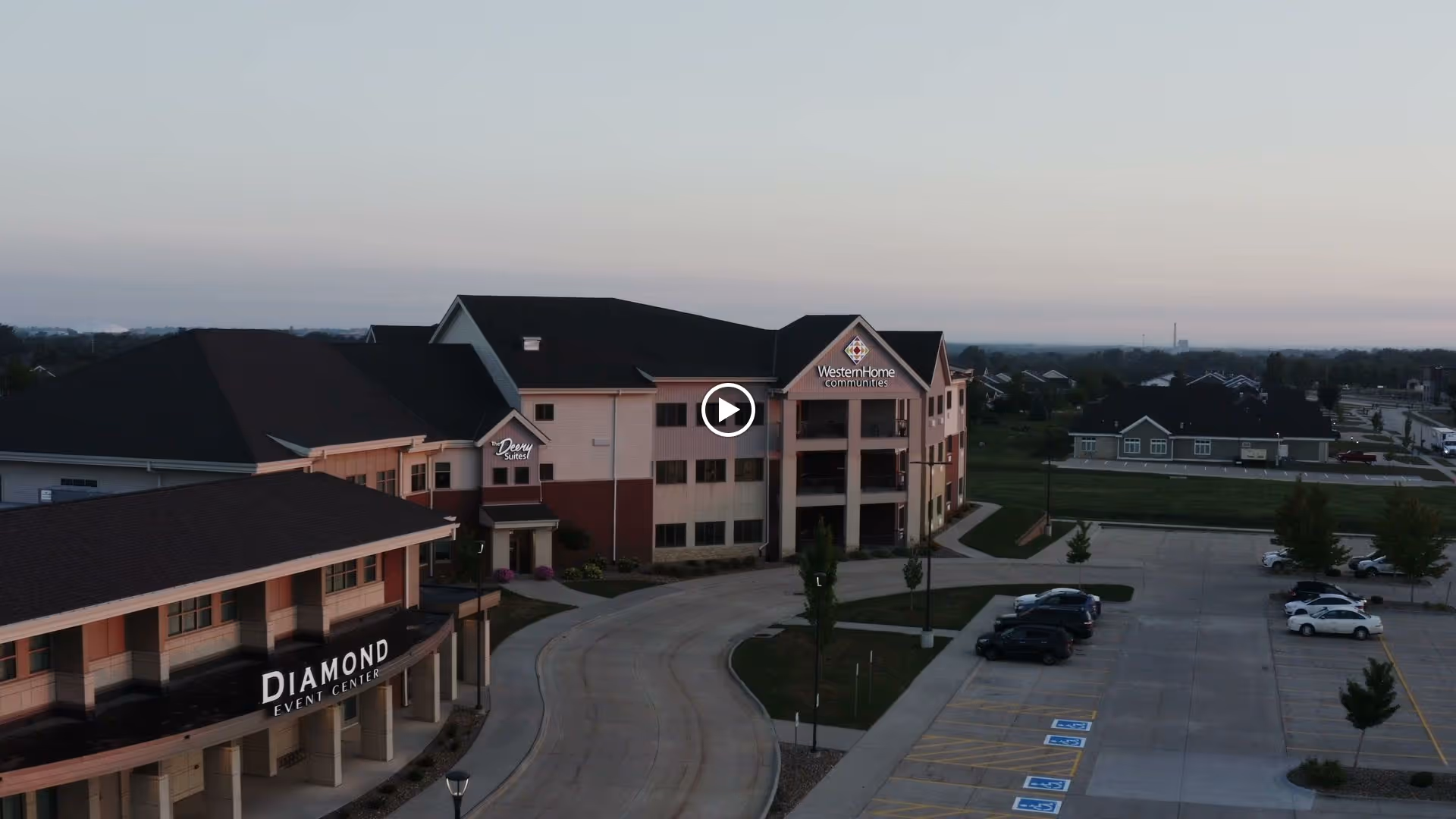 Aerial view of the Western Home Communities building and adjacent Diamond Event Center with parking lot at dusk.