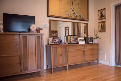 Wooden dresser and tall cabinet with TV in a warmly lit living area.