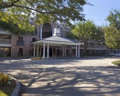 Front entrance of a multi-story brick senior living building with a covered porte-cochère and trees in front.