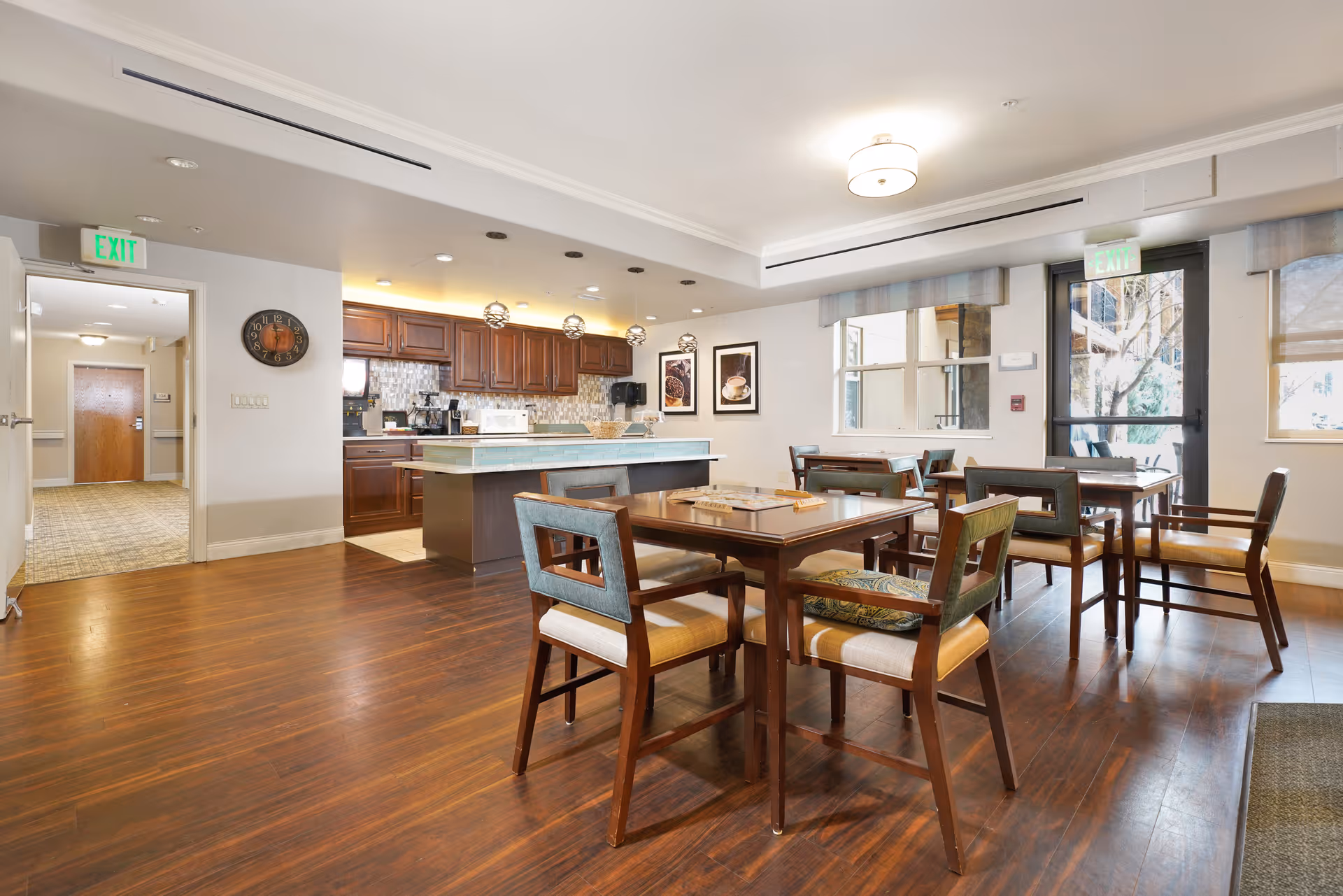 Communal dining area with wooden tables and chairs and a kitchen counter with cabinets in the background.
