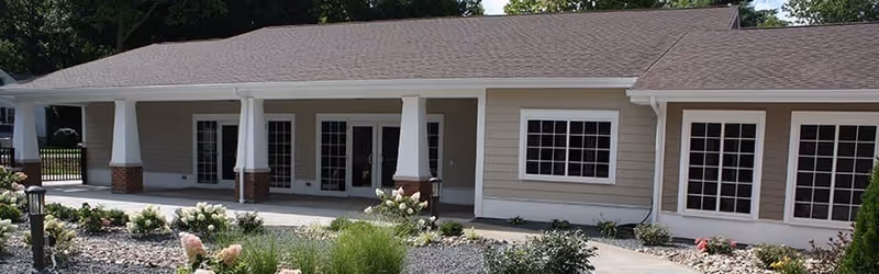 Single-story building exterior with a covered porch supported by columns, multiple glass doors and windows, and a landscaped rock garden in front.